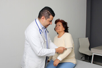 Obraz premium Dark-skinned Latino man medical doctor attends to elderly woman patient performs a reflex check in his office