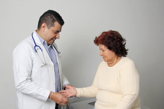 Dark-skinned Latino man medical doctor attends to elderly woman patient performs a reflex check in his office