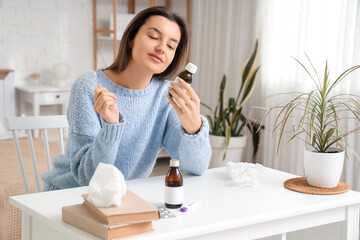 Sick young woman with cough syrup at table in bedroom