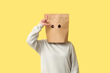 Woman in paper bag showing loser gesture on yellow background