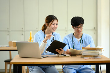 Two medical students in blue scrubs working together on academic tasks at a desk