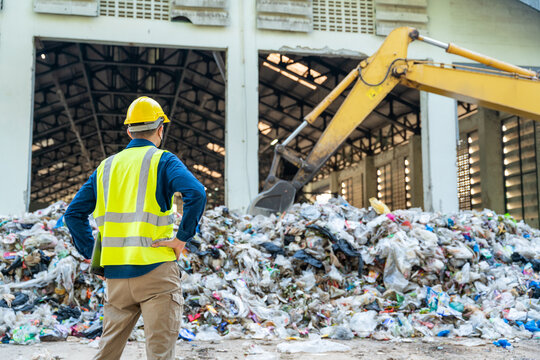 A recycling industry engineer monitoring real-time metrics on a laptop while heavy machinery operates seamlessly at waste separation plant.