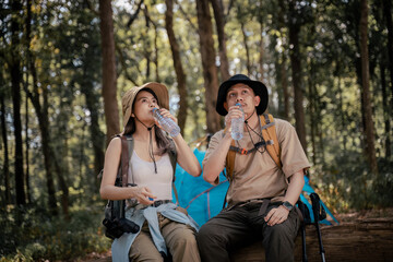 Hikers sitting on a wooden bench in a lush forest setting holding water bottles and appear to be taking a refreshing break during their trek.