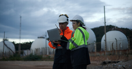 Male project engineers and female chemical engineers are engaged in a discussion regarding safety protocols in the chemical storage tank area at the oil refinery.