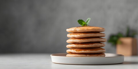 Stacked golden pancakes drizzled with sweet syrup and garnished with a fresh mint sprig served on a simple wooden plate against a gray backdrop