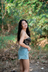 Fototapeta premium Portrait of sexy asian woman in a military print strapless dress, camping in the forest concept.