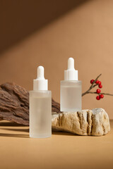 The minimalist cosmetics ad shot shows two frosted glass dropper bottle mockups, placed on a light...