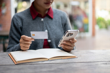 A cropped image of a woman holding a smartphone and a credit card while sitting at an outdoor table.