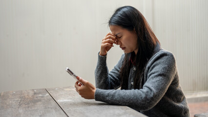A woman struggling with her finances is holding a credit card and looking hopelessly at her phone.