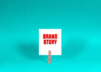 Brand story branding symbol. Concept words Brand story on White Square Paper Held by Wooden Clothespin Green Background. Business Brand story Concept with Copy Space