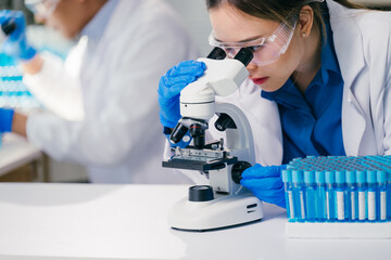 Scientist wearing lab coat and gloves looking through microscope, performing scientific research in modern laboratory with test tubes nearby