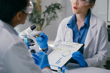 Two scientists wearing lab coats and gloves are analyzing data and charts in a modern laboratory,...