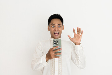 man wearing elegant traditional clothing looks excited while holding a smartphone, expressing...