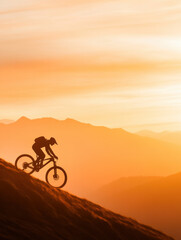 Fototapeta premium Silhouette of cyclist riding downhill at sunset over mountains