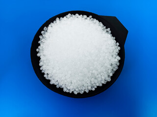 Virgin polymer granules with blue background, virgin homopolymer resin raw material in black cup, suitable for plastic company profile product catalog design
