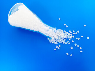 Fototapeta premium Virgin polymer granules with blue background, virgin homopolymer resin raw material poured from glass with blue background, suitable for plastic company profile product catalog design