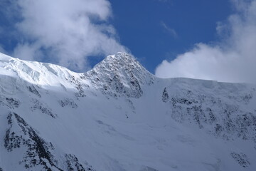 A stunning rock formation covered in snow, set against a clear blue sky with fluffy clouds in the background, creating a peaceful and breathtaking mountain landscape.