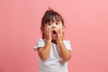 Amazed horrified little three years old girl keeps mouth opened, hands on cheeks, being shocked...