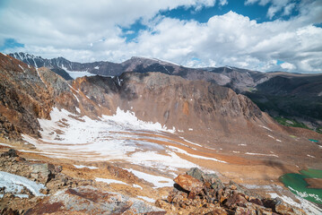 Vast top view from precipice edge to unusual beautiful glacier and glacial lake. Sharp rocky ridge and large mountain range in far away. Atmospheric layer landscape with big hills and high mountains.