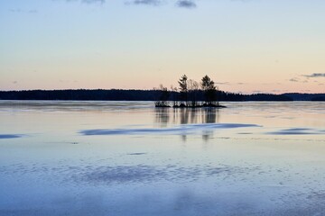 Tranquil winter landscape of a frozen lake with a small island and trees at sunset