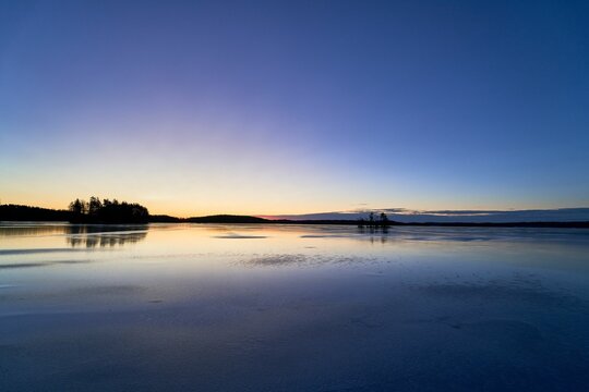 Serene winter sunset over a frozen lake with trees silhouetted against a colorful sky