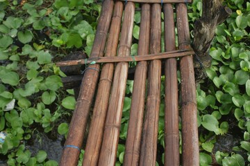 Bamboo Bridge or Wooden Walkway on Water with Green Aquatic Plants Background,  Rustic Natural Structure for Eco-Tourism, Agriculture, or Rural Paths in Wetland or Garden Areas