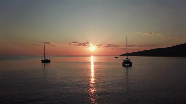 Greece,Tilos Bay,Aerial forward towards open sea and pink sky during sunrise.Silhouettes of boats on anchor,calm sea