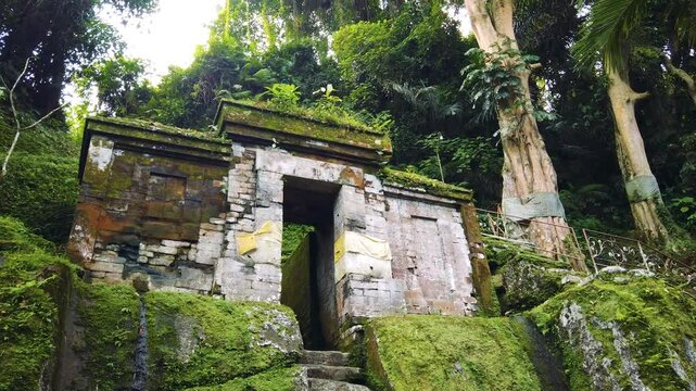 Establishing shot at ancient stone gate, temple entrance of Goa Garba, Bali, Indonesia, around moss, green tropical landscape, religious landmark
