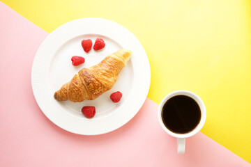 Coffee cup and fresh croissant on yellow and pink background