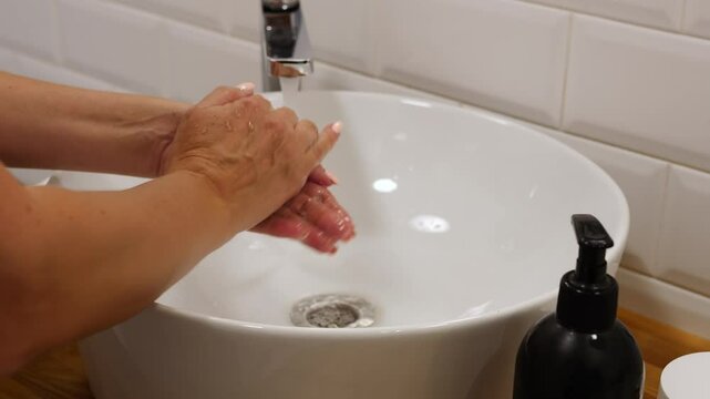 Woman performs her morning ritual washing her hands with soap at sink Captured is regularity of rituals in bathroom for fresh start to day Moment emphasizes importance of cleanliness in everyday life