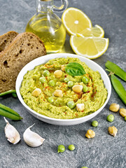 Hummus from green peas in bowl with bread on table