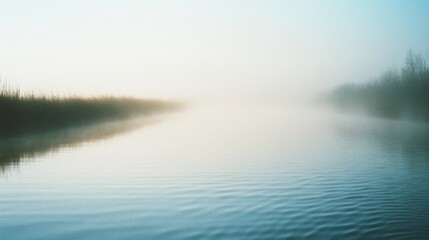 Fototapeta premium A tranquil misty river emerges at dawn, with gentle ripples reflecting the serene morning light, surrounded by hazy silhouettes of distant reeds.