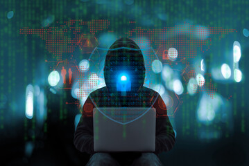 A hooded figure using a laptop surrounded by digital symbols, representing hacking, cybercrime, and global cybersecurity threats. © chartphoto