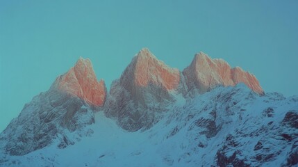 Obraz premium Pointed snow-capped peaks bask in soft, warm hues of dawn light, casting an ethereal glow over the rugged mountain landscape as nature's beauty awakens.