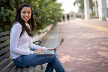 Indian girl, student using laptop at park for education, learning or studying at university on bench in garden. Notebook, serious and woman at outdoor