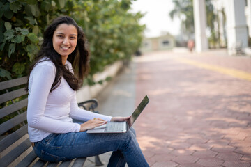 Indian girl, student using laptop at park for education, learning or studying at university on bench in garden. Notebook, serious and woman at outdoor