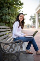 Obraz premium Indian girl, student using laptop at park for education, learning or studying at university on bench in garden. Notebook, serious and woman at outdoor