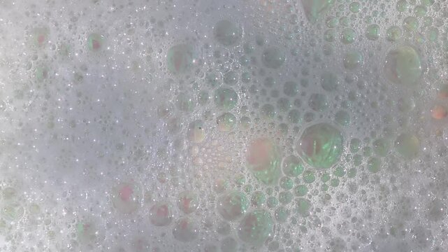 Bubbles rise and form a frothy texture in soapy water while dishes are being washed in a kitchen setting.