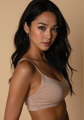 Naklejka premium Portrait of a slender woman in a sport bra, with medium black wavy hair, confidently posing in a seductive manner. The beige background and realistic lighting enhance the detailed texture of her skin