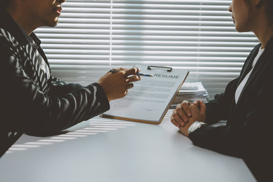 Employer pointing at a resume with a pen while interviewing a candidate in a bright, modern office, fostering a professional atmosphere for discussion and evaluation