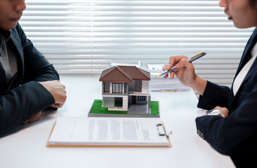 Real estate agent showing house model to client during a meeting discussing terms and conditions of...