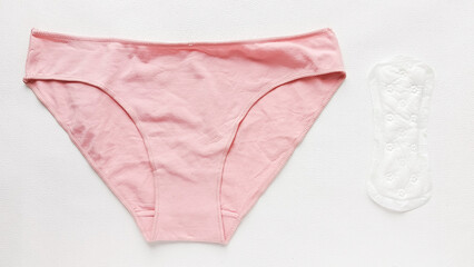 Women's pink panties and disposable pad on the table. Comparison of reusable menstrual panties and disposable pads. Allergy to pads. Hygiene products. Monthly cycle. © Ira