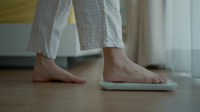 Close up a woman's bare feet stepping onto a digital weighing scale in the morning at home. Healthy lifestyle and weight awareness concept