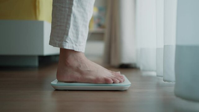 Close up a woman's bare feet stepping onto a digital weighing scale in the morning at home. Healthy lifestyle and weight awareness concept