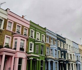 The iconic houses of Notting Hill stand proudly, showcasing vibrant pink, green, blue, and white facades under a cloudy sky, with no people in sight.