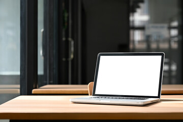 Laptop with white empty screen on a wooden desk in modern office