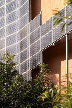 Solar panels gleaming on the side of a building are integrated within a lush, green environment, symbolizing the harmony between urban infrastructure and nature.