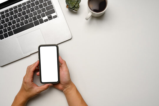 Above view of hands holding a smartphone with blank screen on white desk - Powered by Adobe
