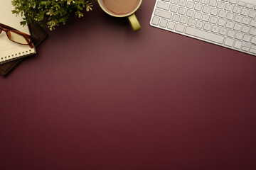 Stylishly workspace with keyboard, a cup of coffee, plan notebook on maroon background