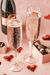 Glasses of champagne, champagne bottle and praline gift box. Surrounded by heart shaped chocolates. Isolated on pink background. Valentine's day, Greetings, Valentine, Gift, Surprise.